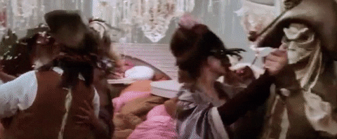 Fantasy ballroom scene in which Sarah wears a white, glittering dress and dances with Jareth, who wears a black glittering prince's outfit with white cravat. They are surrounded by grotesque masquerade masked dancers and Sarah looks worried.