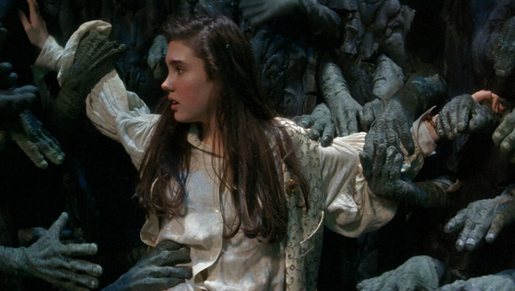 A teenage girl with long brown hair, wearing a cream shirt and waistcoat is held by hundreds of strange green hands as she falls down a pit.