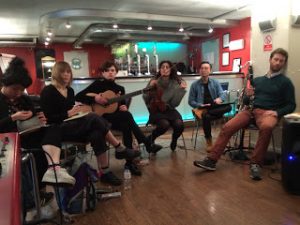 Musicians sat in the bar of a London club, jamming with various instruments.