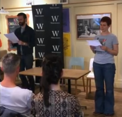 A young man with a beard and a young woman with short red hair read poetry in a Waterstones bookshop
